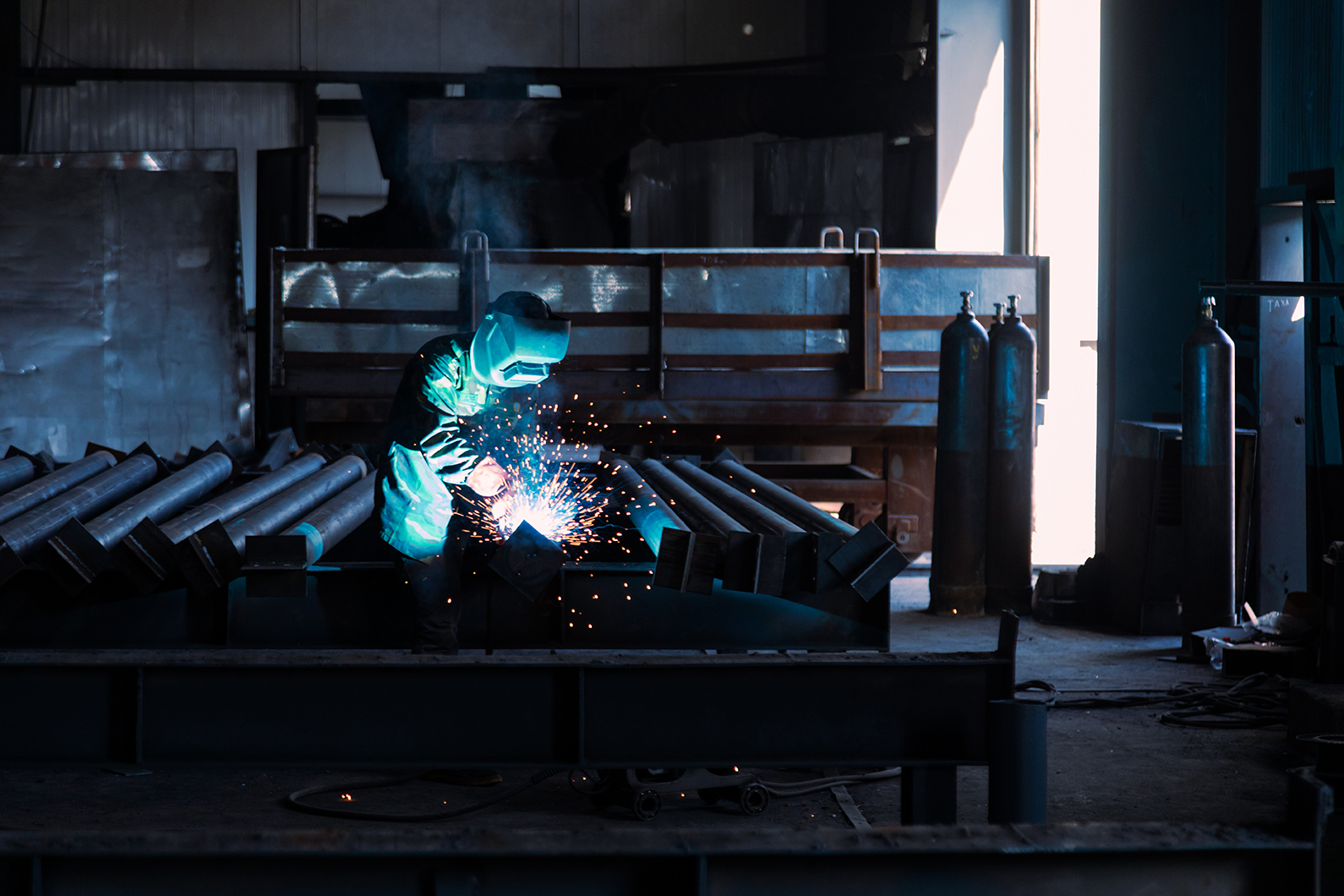 Industrial welder with a torch and protective helmet welding metal profiles in factory