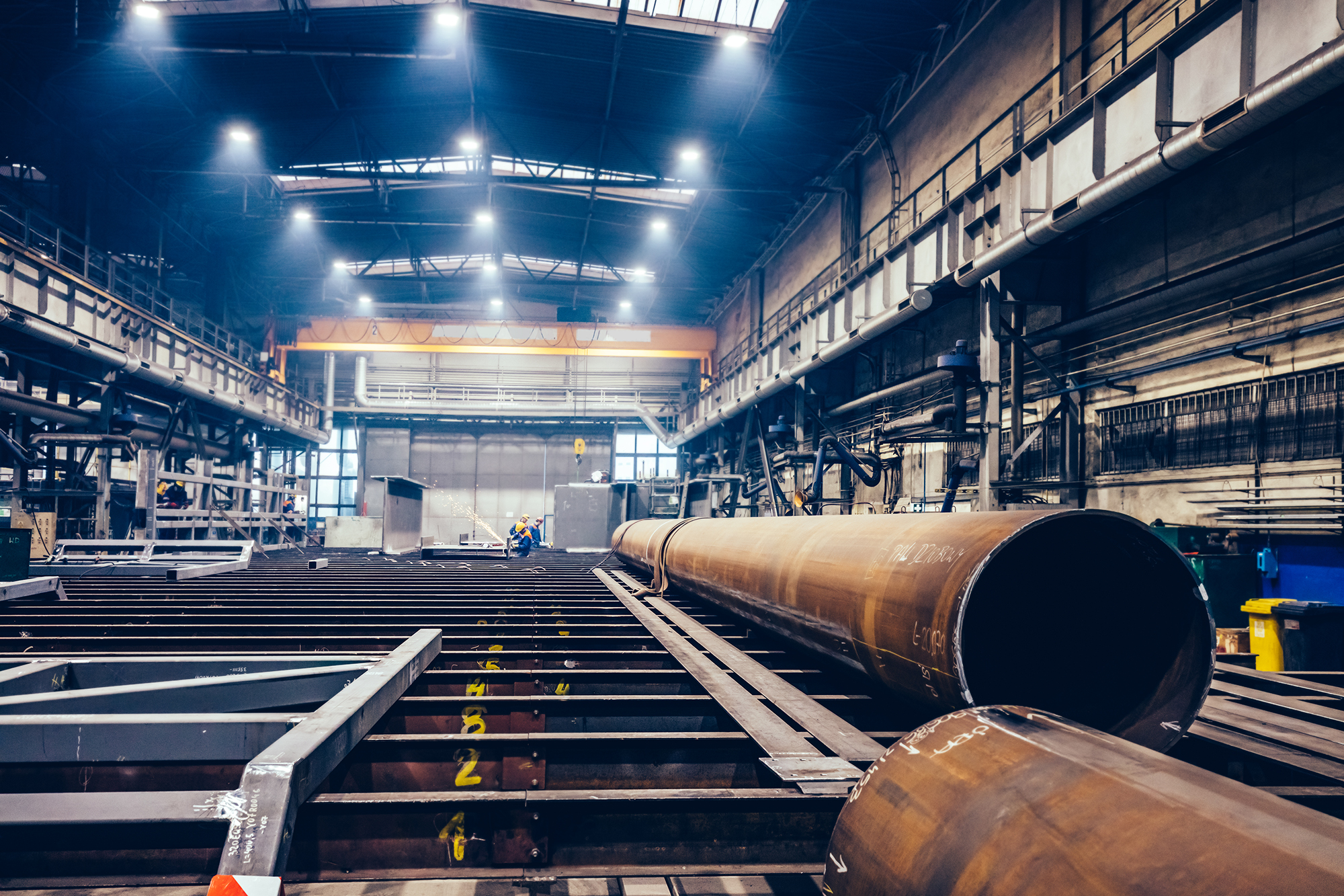 Pipes and steel profiles in a big factory. Workers welding. Shipyard, heavy industry